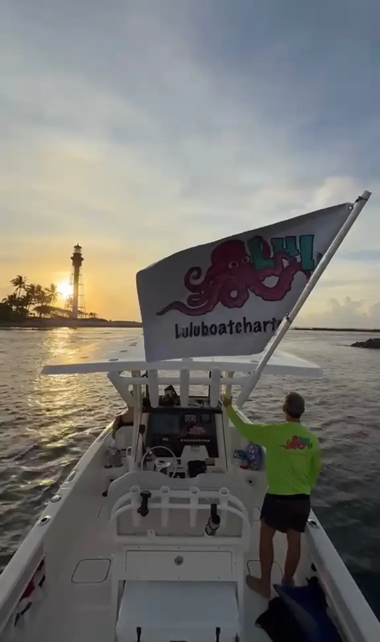 Captain waving the Lulu Boat Charter flag at Hillsboro Lighthouse at sunset