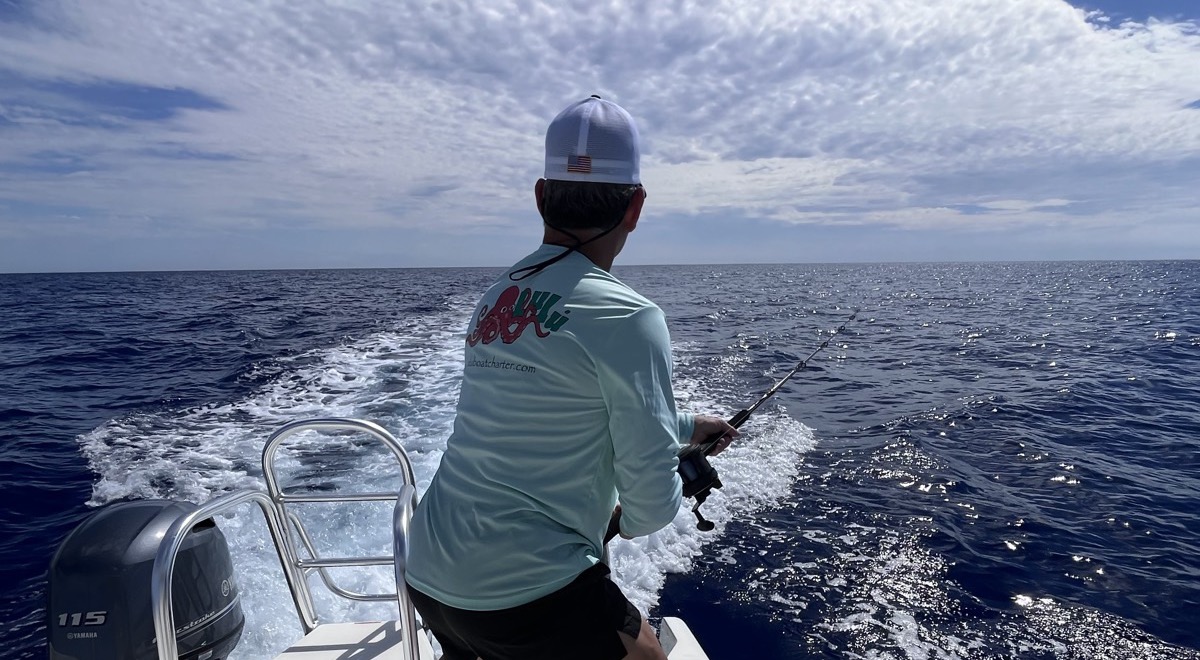 Angler working a rod off the stern during an offshore fishing charter with Lulu Boat Charter